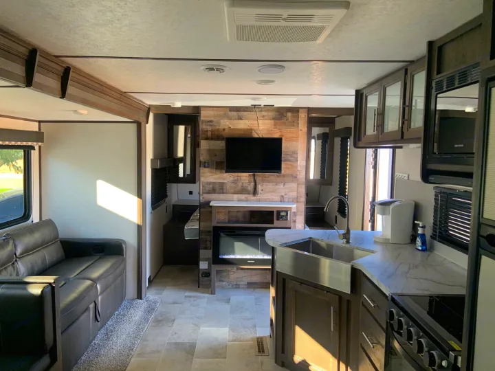Spacious, modern RV rental interior featuring a comfortable living area with couch, a full kitchen, and an entertainment center with fireplace.. Dutchmen Coleman Lantern 2021