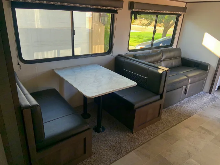 Spacious RV rental interior: dining table with leather benches, plus a comfy sofa. Scenic windows.. Dutchmen Coleman Lantern 2021