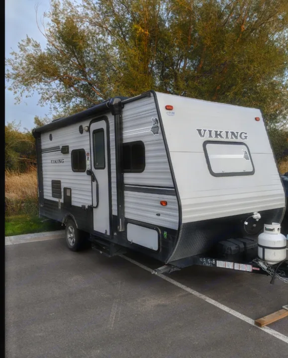 This light gray Viking travel trailer, ideal for an RV rental adventure, is parked on asphalt with trees behind it.. Forest River Viking 2018
