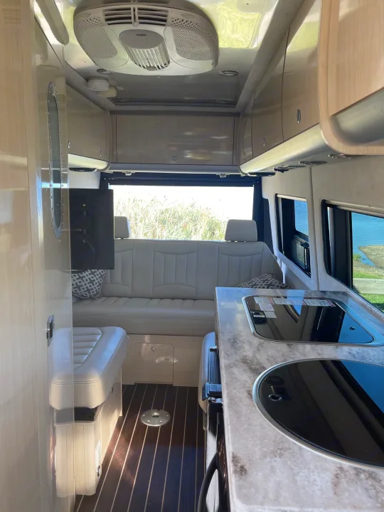 This RV rental's modern interior features a kitchen with built-in cooktops, comfortable seating, and large windows revealing scenic views.. Airstream Interstate 2018