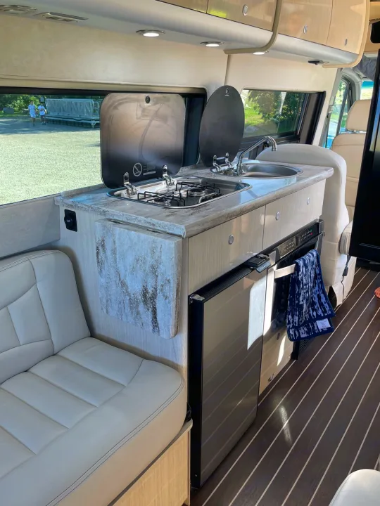 Modern RV rental interior with compact kitchen, sink, stove, fridge, and cozy seating. Perfect for road trips and adventure.. Airstream Interstate 2018