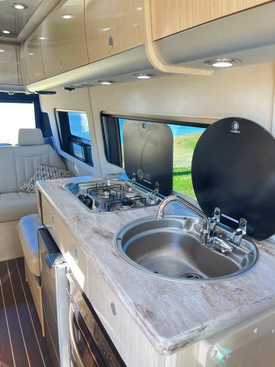Inside this RV rental, find a compact kitchen with a sink, two-burner stove, and comfortable bench seating, ready for adventure.. Airstream Interstate 2018