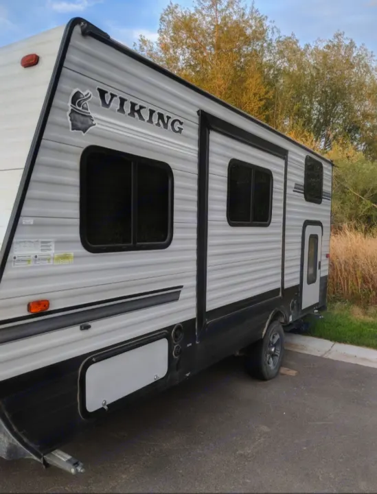 A grey "Viking" travel trailer, great for RV rental and camping, parked on asphalt with trees in the background.. Forest River Viking 2018