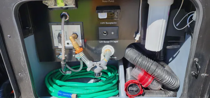An RV rental's exterior utility panel for water, power, and waste hookups, with hoses and a water filter.. Bounder Bounder Motorhome 2021