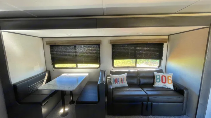Explore this RV rental's comfortable living area, featuring a cozy dining booth and sofa with windows.. Aspen Trail LE 2022