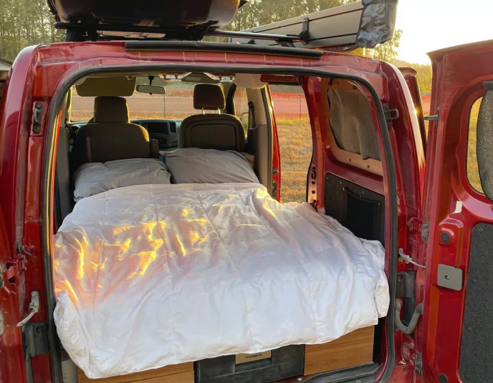 Sleep comfortably in this red **rv rental**. Inside, a cozy bed with white linens awaits your **van life** trip.. Nissan Elgrand 2021