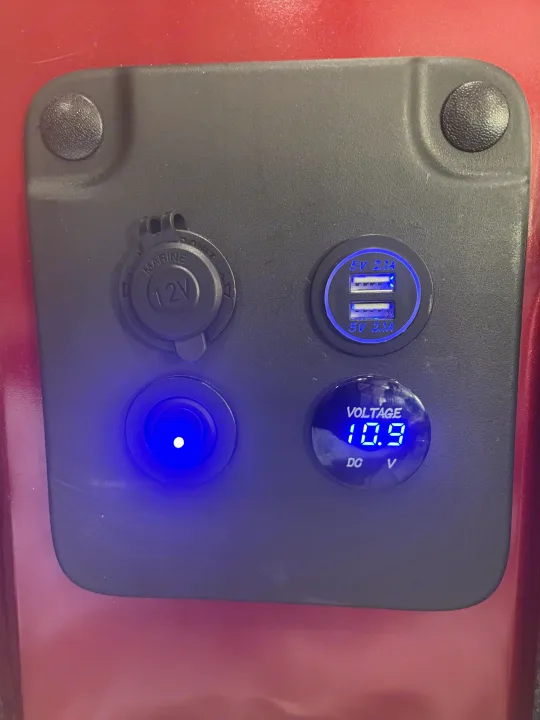 RV rental power panel: glowing blue 12V outlet, dual 5V 2.1A USB, lit button, & 10.9V DC voltmeter.. Nissan Elgrand 2021