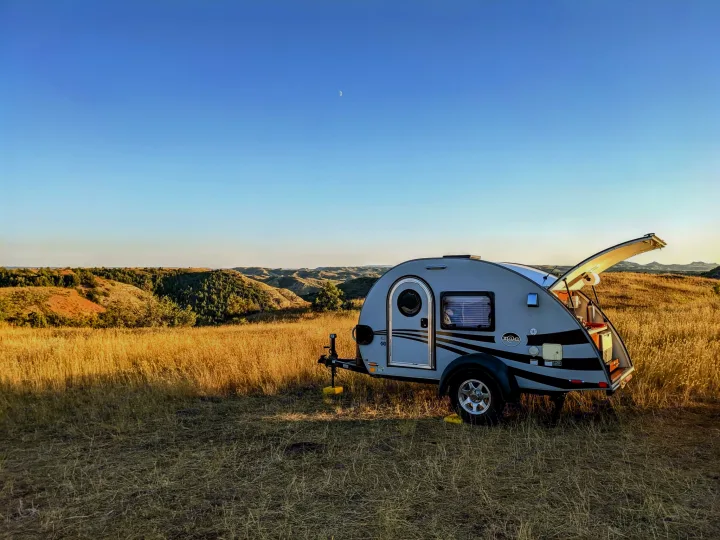 Teardrop RV rental parked in a sunny golden field with rolling hills, perfect for outdoor camping adventures.. T@G XL 2016