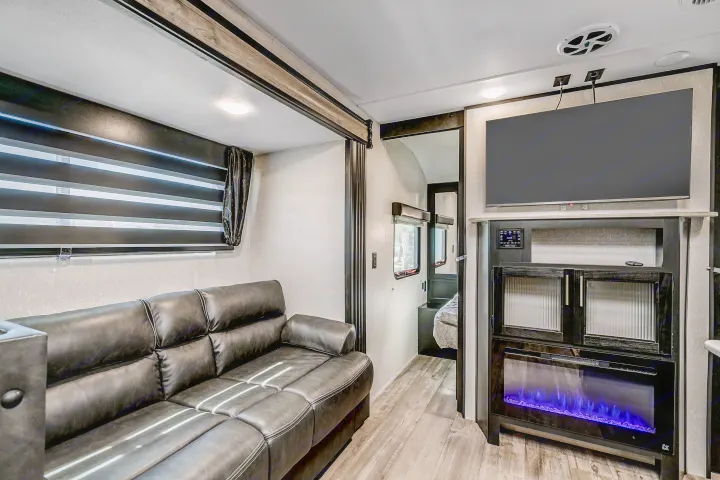 Inside an RV rental: a modern living area with dark leather sofa, large TV, and electric fireplace featuring blue flames.. Cherokee Grey Wolf 2022