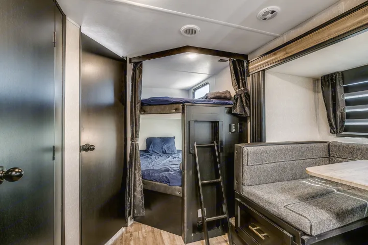 Inside this RV rental: a modern interior with bunk beds, privacy curtains, and a U-shaped dining booth, offering comfort for your journey.. Cherokee Grey Wolf 2022