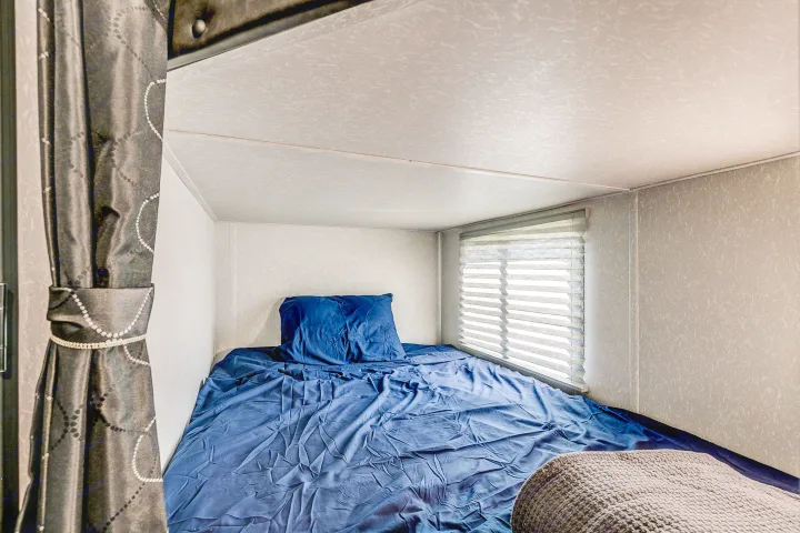 Cozy RV rental bunk with blue bedding and window blinds, offering a compact sleeping space.. Cherokee Grey Wolf 2022