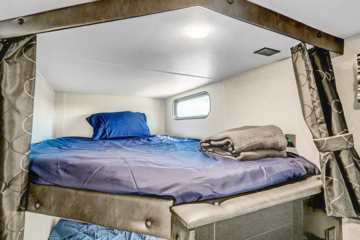 Inside an RV rental: A well-lit bunk bed with blue bedding, a small window, and grey blanket.. Cherokee Grey Wolf 2022