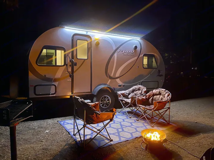 RV rental campsite at night: illuminated R-Pod trailer, cozy fire pit, and camping chairs on a rug for relaxation.. R-Pod R-Pod Trailer 2021