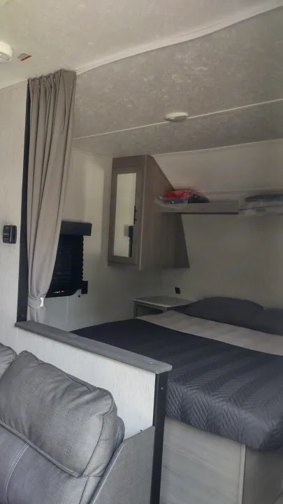 Inside an RV rental: A compact, modern bedroom area with a bed, nightstand, and window blinds, designed for efficient use of space.. Dutchmen Coleman Lantern LT 2022