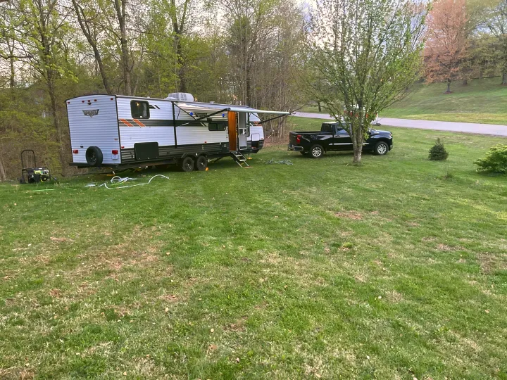Outdoor RV rental setup with a white travel trailer, black pickup, and generator on a grassy campsite.. Forest River Wildwood X-Lite 2020