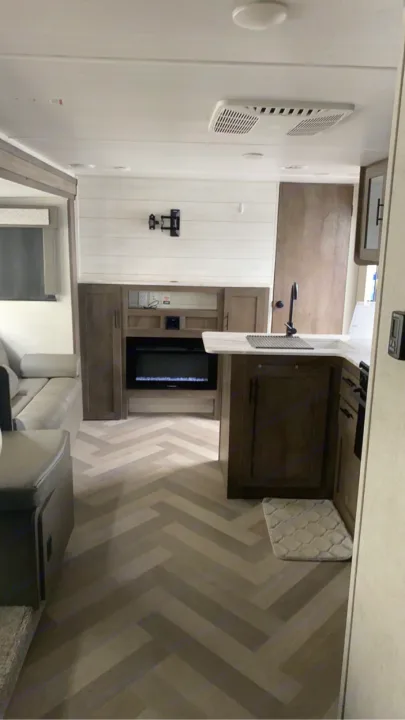 Modern RV rental interior with a cozy living area, kitchen, electric fireplace, and chevron pattern flooring.. Forest River Wildwood X-Lite 2020