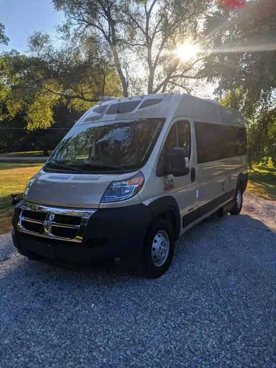 Tan rv rental van parked on a gravel driveway with sunlit trees. Ideal for your next outdoor adventure.. Roadtrek Roadtrek Class B 2017