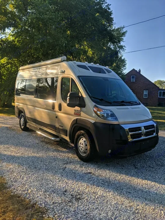 A modern, light-colored Ram ProMaster camper van, perfect for an rv rental adventure, parked on a gravel lot under sunlight.. Roadtrek Roadtrek Class B 2017