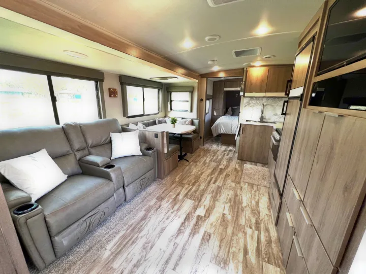 Inside this modern rv rental, find a bright living area, comfy recliners, dinette, kitchen, and a glimpse of the bedroom.. Grand Design Imagine 2021