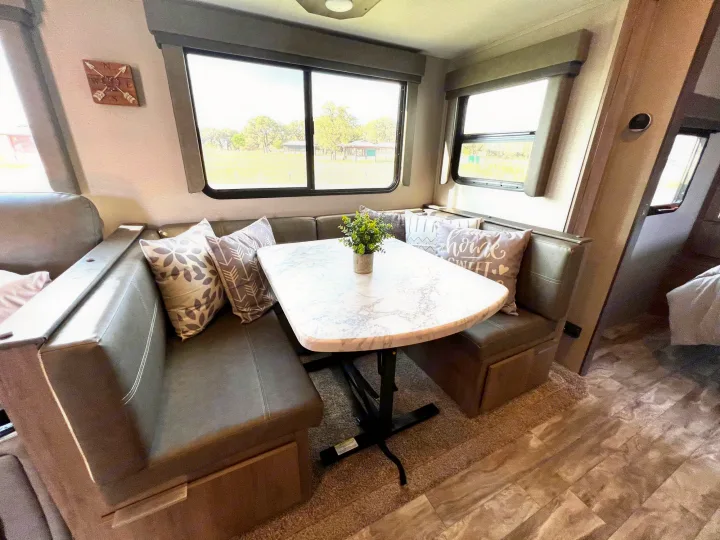 RV rental interior featuring a cozy dinette with a marble table, bench seating, and scenic window views in a camper.. Grand Design Imagine 2021