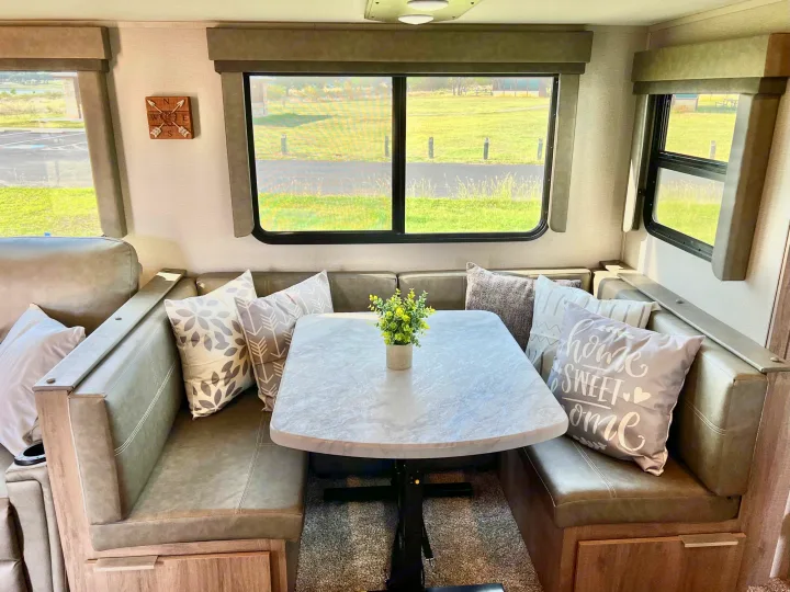 Spacious RV rental dinette featuring a table, plush booth seating, and scenic windows overlooking a green landscape.. Grand Design Imagine 2021