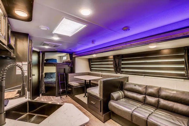 RV rental interior: kitchen sink, bunk beds, dining table, and sofa. Brightly lit with purple ceiling lights.. Cherokee 26DBH 2022