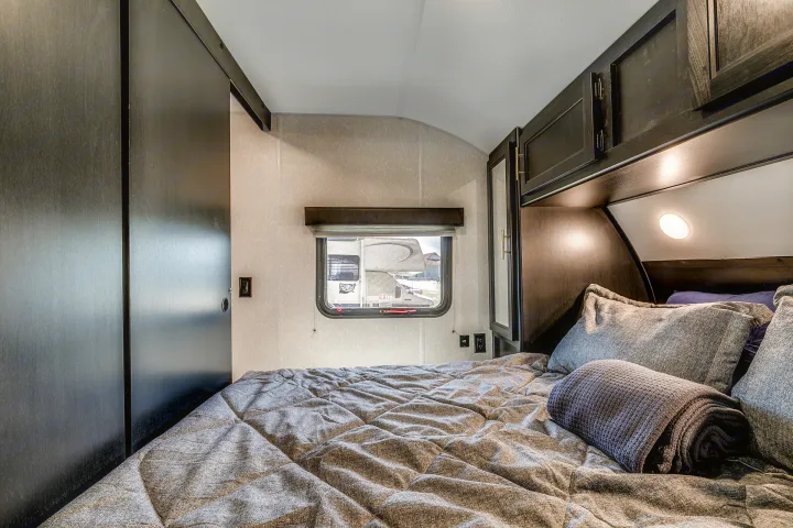 Cozy RV rental bedroom featuring dark wood cabinets, a quilted bed, window, and built-in lighting.. Cherokee 26DBH 2022