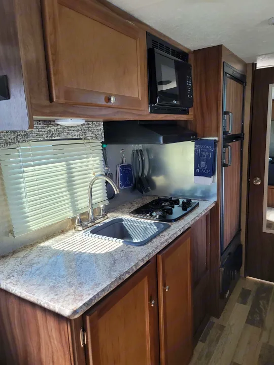 Compact RV rental kitchen featuring a sink, stovetop, microwave, and refrigerator, illuminated by natural light.. Forest River Viking 2018