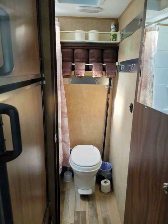 Compact **RV rental** bathroom with toilet, neatly stacked towels, shower curtain, and essential toiletries/supplies.. Forest River Viking 2018