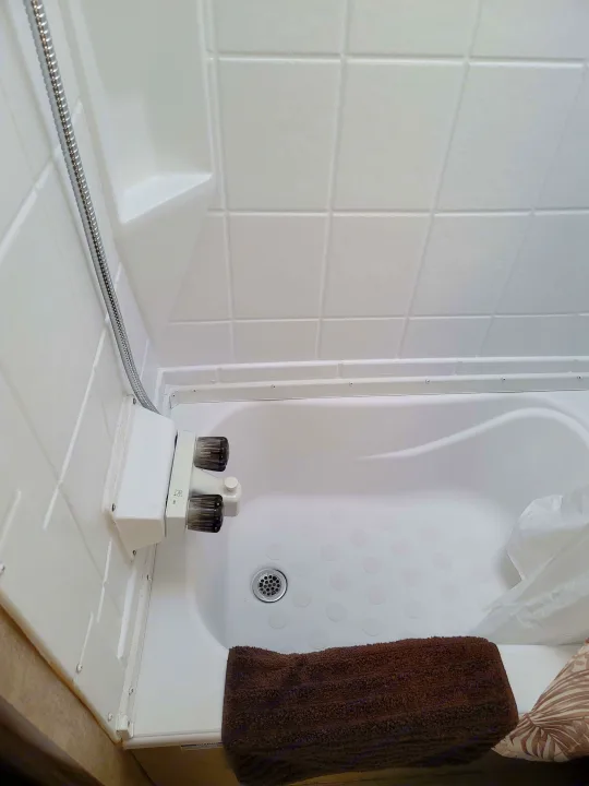 This RV rental features a compact, white molded shower and tub with a flexible hose, dual controls, and a brown towel in the basin.. Forest River Viking 2018