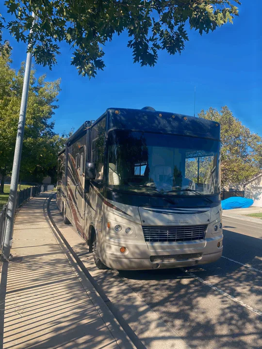 Front view of a Georgetown RV rental, tan & black, parked roadside under trees on a sunny day.. Forest River Georgetown 2011