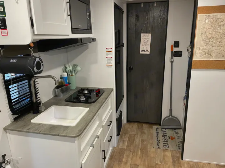 Compact RV rental kitchen showing a sink, stovetop, microwave, and cabinets, ideal for camping adventures.. Keystone RV Hideout 2022