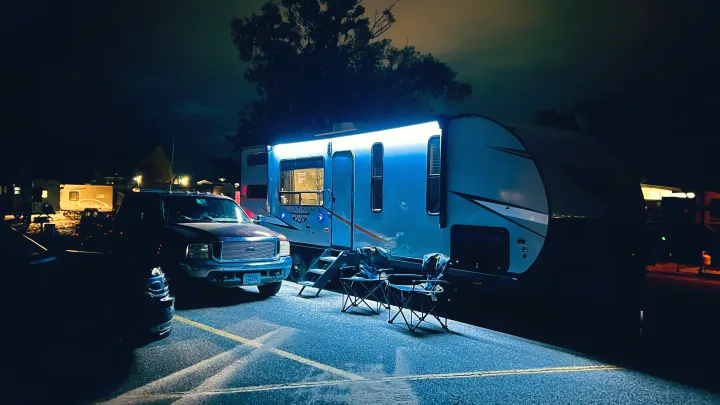 Nighttime RV rental setup: Illuminated travel trailer, tow truck, and camping chairs ready for a cozy camp evening.. Forest River Wildwood 2022