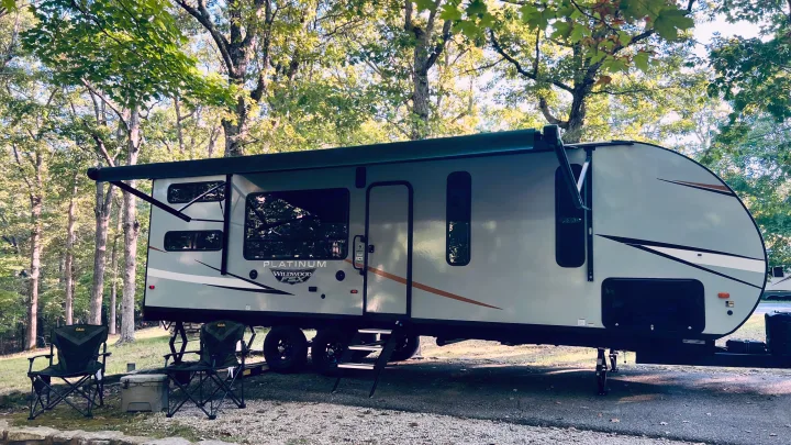 This Platinum Wildwood FSX RV rental is perfectly set up at a leafy campground, complete with chairs and a cooler.. Forest River Wildwood 2022
