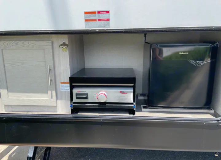 RV rental outdoor kitchen featuring a Suburban griddle, Hotpoint mini-fridge, a storage cabinet, and bottle opener.. Forest River Coachmen Catalina Legacy 2022