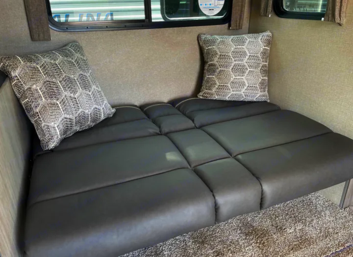 RV rental interior: a grey segmented bench/bed with two patterned pillows, offering comfortable seating and sleeping space.. Forest River Coachmen Catalina Legacy 2022