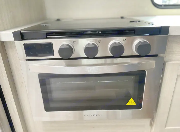 Stainless steel Greystone RV stove & oven, seen in an RV rental kitchen. Features a 4-burner cooktop and digital display.. Forest River Coachmen Catalina Legacy 2022