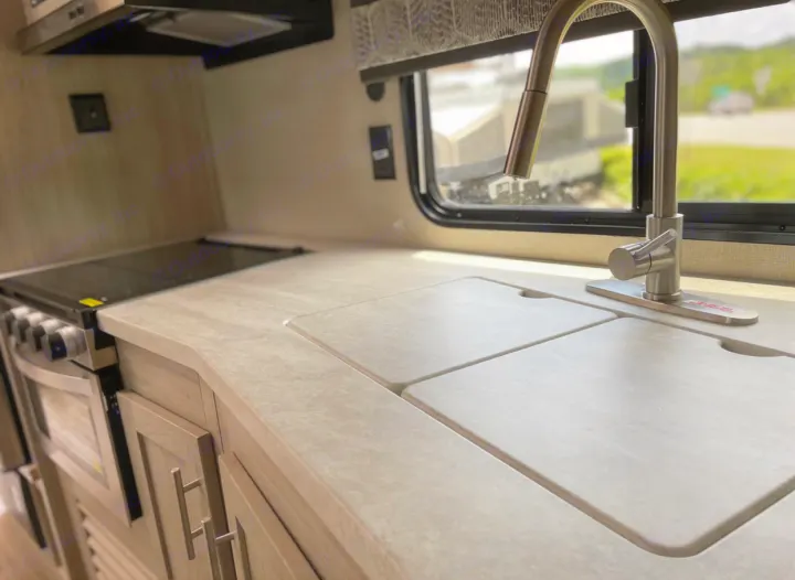 RV rental kitchen features a modern sink with covers, pull-down faucet, and cooktop with oven, ideal for compact living.. Forest River Coachmen Catalina Legacy 2022