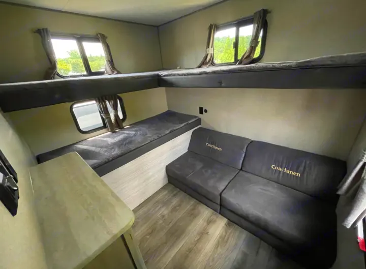 RV rental interior featuring L-shaped bunk beds, a lower bench bed with a window, and a dark "Coachmen" sofa.. Forest River Coachmen Catalina Legacy 2022
