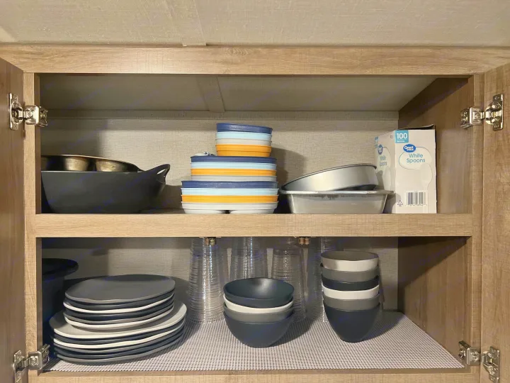 Organized RV rental cabinet: stackable dishes, bowls, cups, and cooking pans, optimized for compact living.. Grand Design Imagine 2021