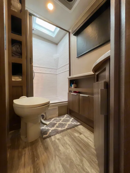 Inside an RV rental: a modern bathroom featuring a walk-in shower with a skylight, toilet, and vanity cabinet.. Grand Design Imagine 2021