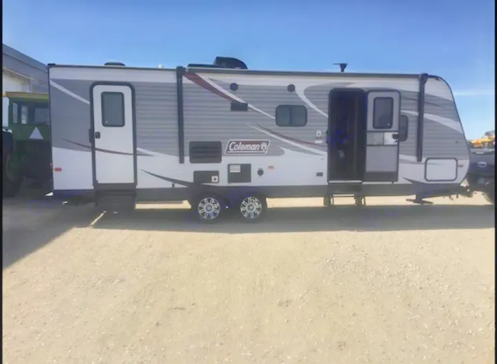 A modern gray and white travel trailer, ideal for rv rental, is parked on gravel. It has two entry doors and multiple windows.. Dutchmen Coleman Lantern 2017