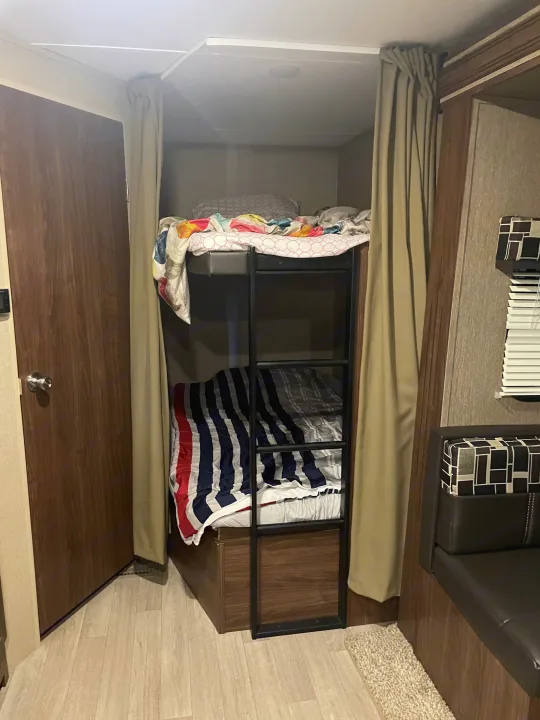 Cozy RV rental bunk beds with privacy curtains and a ladder are neatly arranged in a compact, wood-paneled interior.. Dutchmen Coleman Lantern 2017