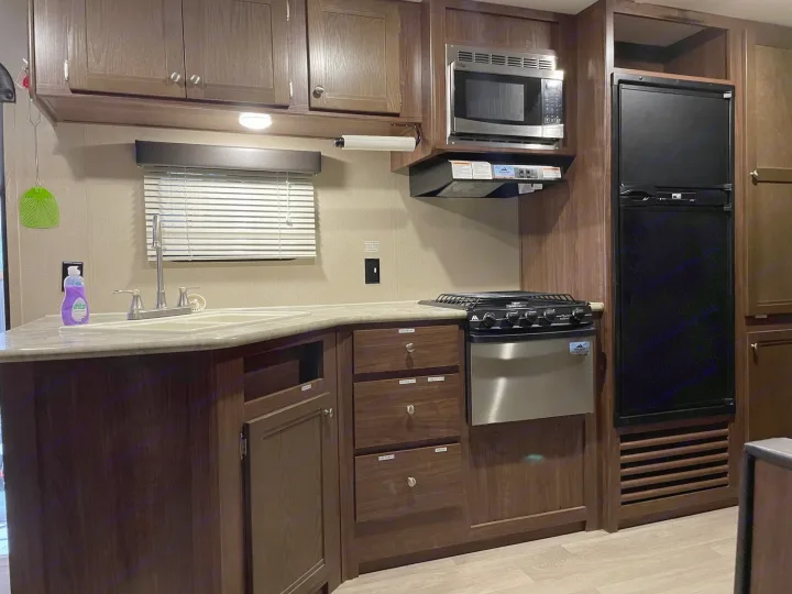 RV rental kitchen showcasing dark wood cabinets, a sink, stainless steel microwave, stove, and refrigerator.. Dutchmen Coleman Lantern 2017