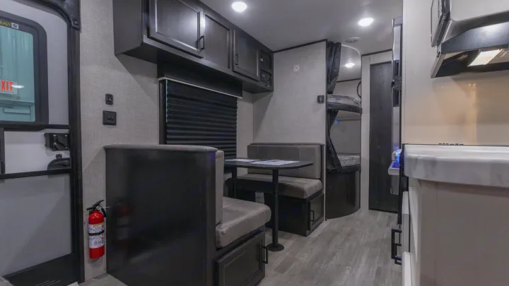 RV rental interior showcasing a compact dinette with table, bunk beds, and kitchen area. Features overhead cabinets & wood floor.. Jayco Jay Flight SLX 2022