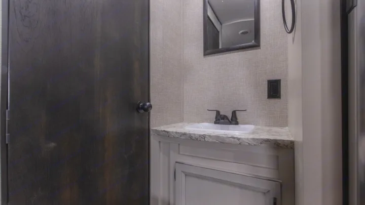 Inside a compact RV rental bathroom: dark door, textured walls, vanity with sink, marble-look counter, and mirror.. Jayco Jay Flight SLX 2022