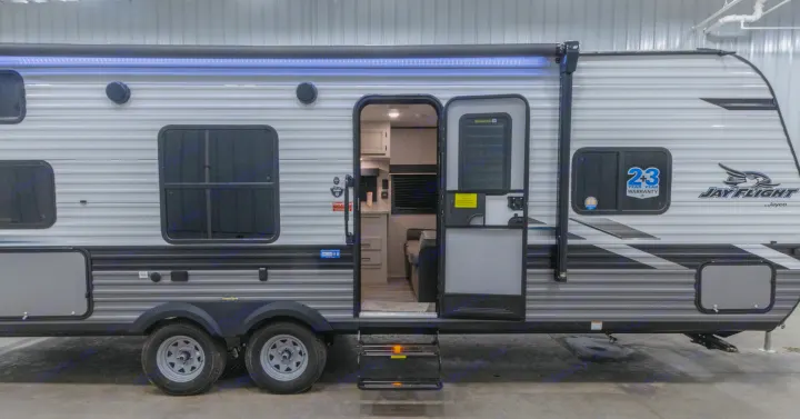 Side view of a Jay Flight travel trailer RV for rv rental, featuring an open door revealing the cozy interior and a lit LED awning.. Jayco Jay Flight SLX 2022