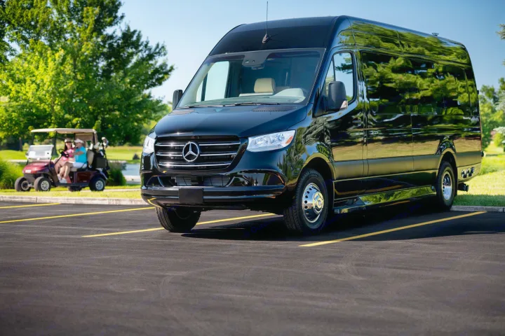 Black Mercedes-Benz Sprinter RV rental, gleaming, parked on asphalt. A golf cart with two people is in the background.. Ultimate Toys Ultimate Coach 2023