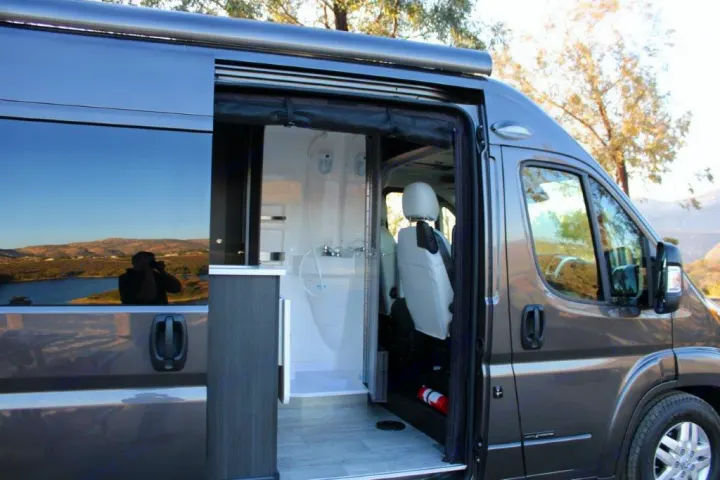 Grey RV rental with its side door open, revealing a compact interior featuring a shower and front passenger seat.. Roadtrek Zion 2022