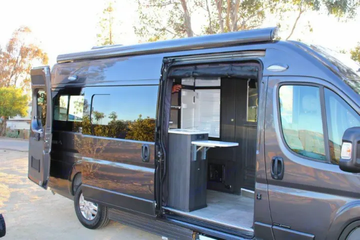 Open gray camper van RV rental, showing its interior kitchen with a fridge, sink, and pull-out table for comfortable travel.. Roadtrek Zion 2022